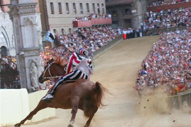 I cavalli del Palio di Siena in corsa in Piazza del Campo davanti alla folla